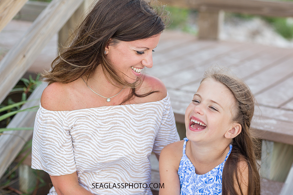 Mom and daughter sit and laugh on the board walk on the beach during a family photo shoot in Vero Beach Florida