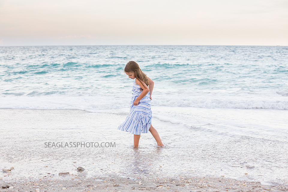 Little girl looks for shells through the oceans water during a family photo shoot in Vero Beach Florida