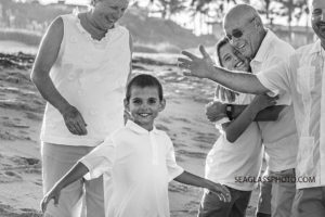 Close up black and white photo of a little boy smiling on th beach surrounded by family during a family photo shoot in Vero Beach Florida