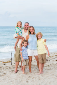 Family of five hug for a pic in front of the ocean during family photo shoot in Vero Beach Florida