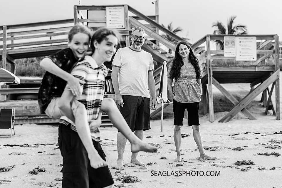 Black and white photo of parents watching their sons play on the beach during family photo shoot in Vero Beach Florida