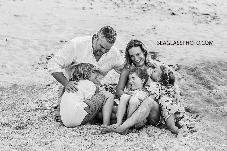 Black and white photo of a family sitting and laughing on the beach during family photo shoot in Vero Beach Florida