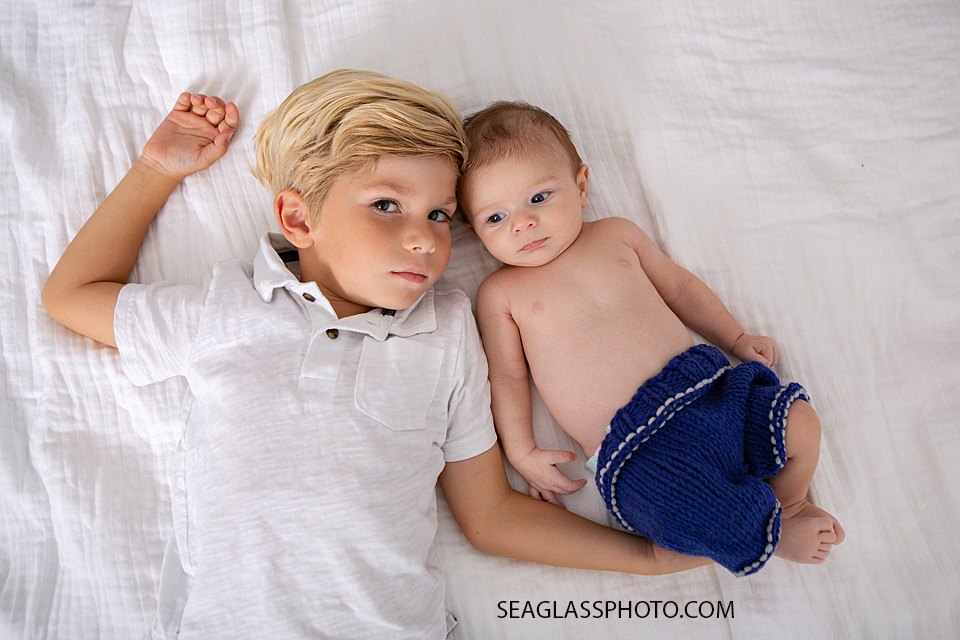 Big brother and little brother lay next to each other during newborn session in Downtown Vero Beach Florida