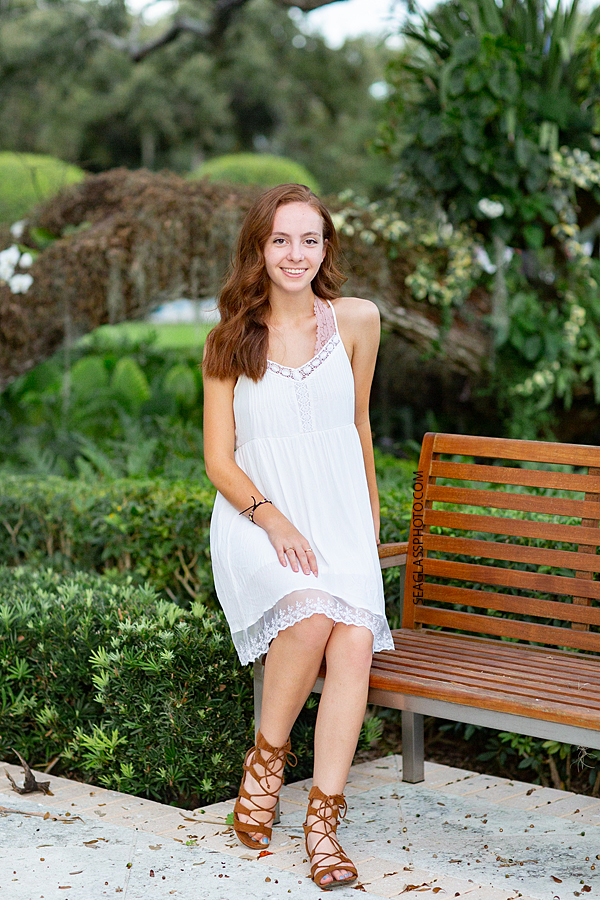 Young senior sits on a bench in Riverside Park during senior photo shoot in Vero Beach Florida