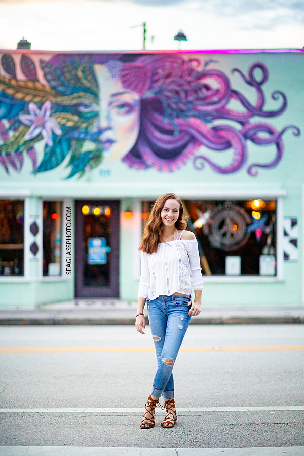 Senior poses in front of a mermaid painting in Down Town Vero during her senior session in Vero Beach Florida