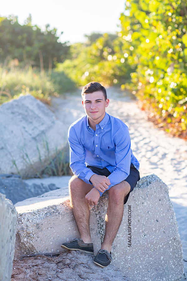 Young man sits on a pile of rocks during his senior pictures in Vero Beach Florida