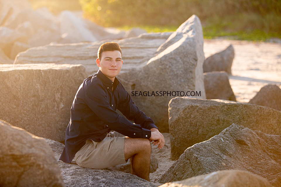 Senior sits on rocks on the beach during his senior pictures in Vero Beach Florida