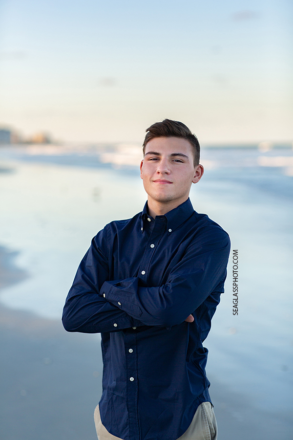 Young man stands on the beach by the ocean during his senior pictures in Vero Beach Florida