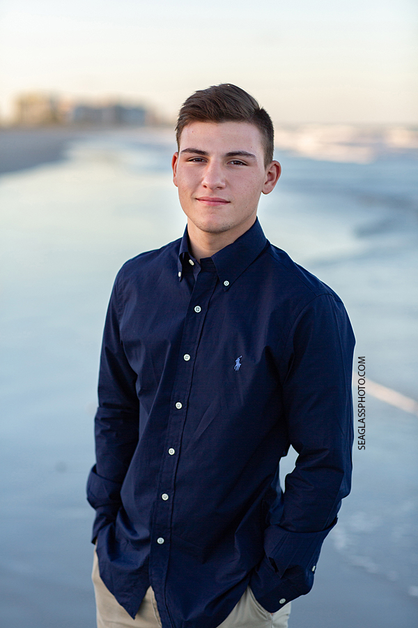 Young man stands on the beach by the ocean during his senior pictures in Vero Beach Florida