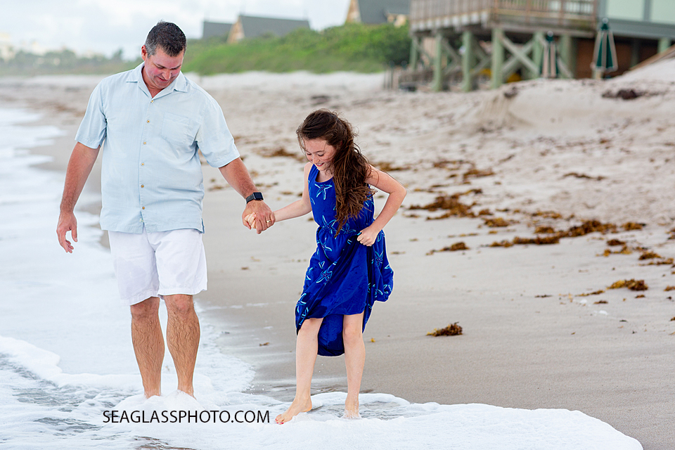 Father and daughter hold hands while walking in the water during family photos in Vero Beach Florida