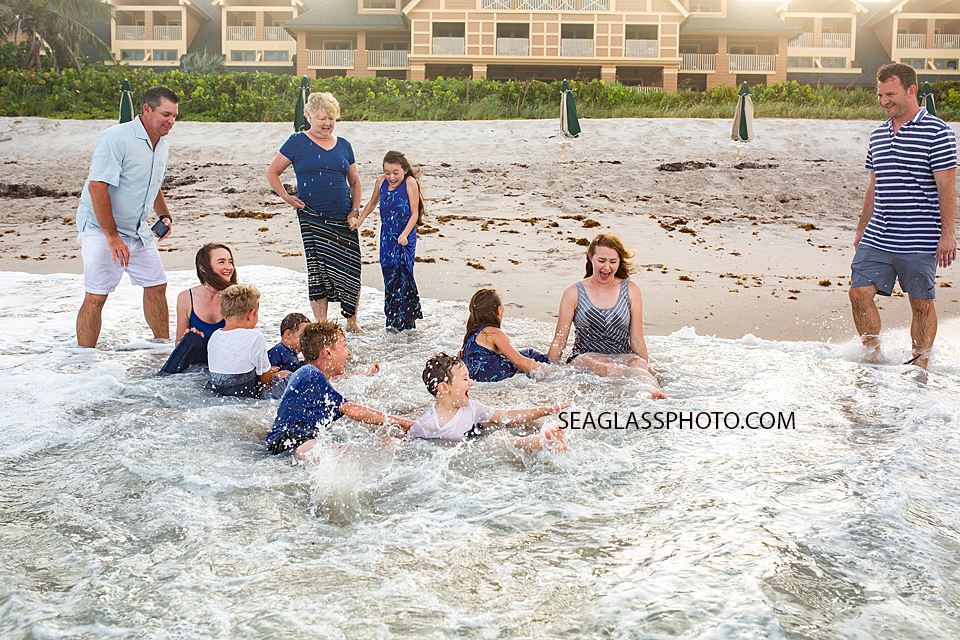 Family gathers and sits in the waves of the ocean during family photos in Vero Beach Florida