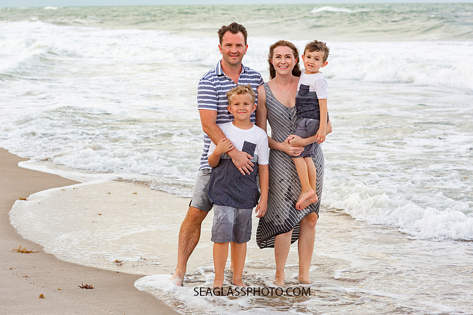 Family of four gather in the waves of the ocean for a family photo during family photos in Vero Beach Florida