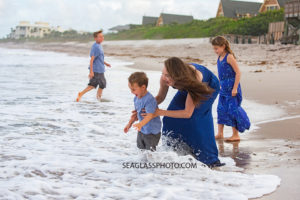 Mother holds son in the waves of the ocean during family photos in Vero Beach Florida