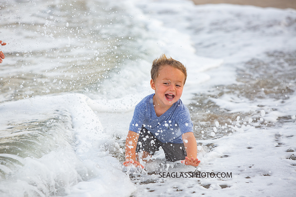 Young boy crawls in the waves of the ocean during family photos in Vero Beach Florida