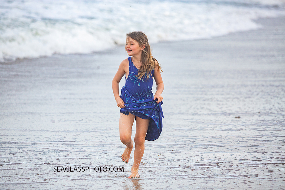 Young girl runs on the beach trying to get away from the water during family photos in Vero Beach Florida