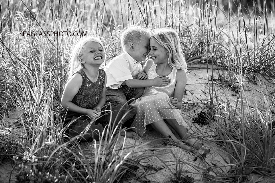 Black and white photo of young siblings sitting and laughing in the duns on the beach during family photos in Vero Beach Florida