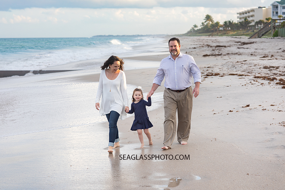 Family of three walks on the beach during family photos in Vero Beach Florida
