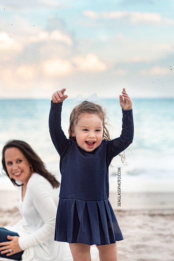 Young girl plays with the sand on the beach like its snow during family photos in Vero Beach Florida