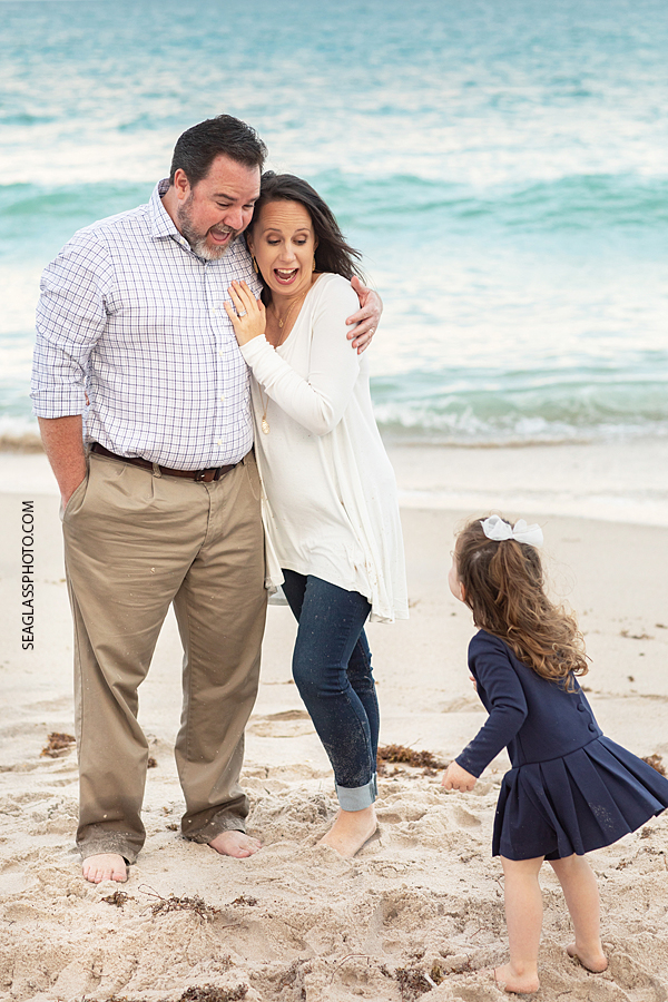 Parents play with their daughter as she pretends to through sand at them on the beach during family photos in Vero Beach Florida