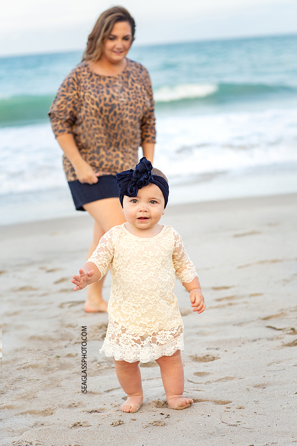 Little girl walking on the beach with her mom behind watching during their family photoshoot in Vero Beach Florida