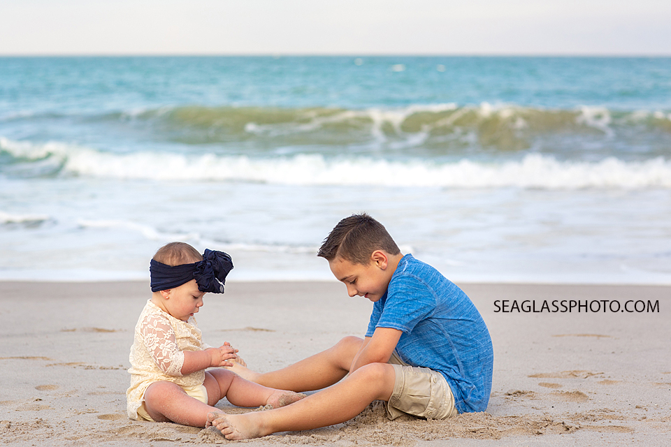 Brother plays with his little sister in the sand on the beach during their family photoshoot in Vero Beach Florida