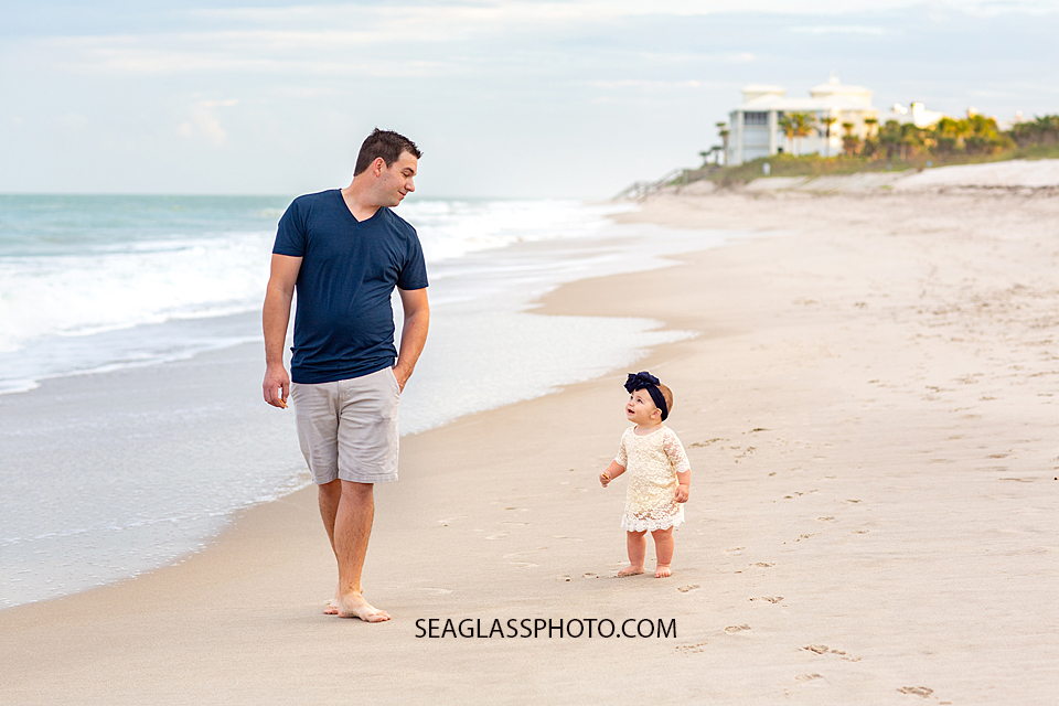 Father walks the beach with his little girl smiling up at him during their family photoshoot in Vero Beach Florida