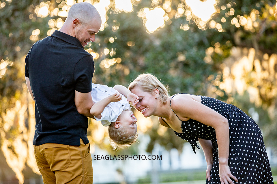 Father holds his son upside down while mom goes in for a kiss on the cheek during family photos at Riverside in Vero Beach Florida