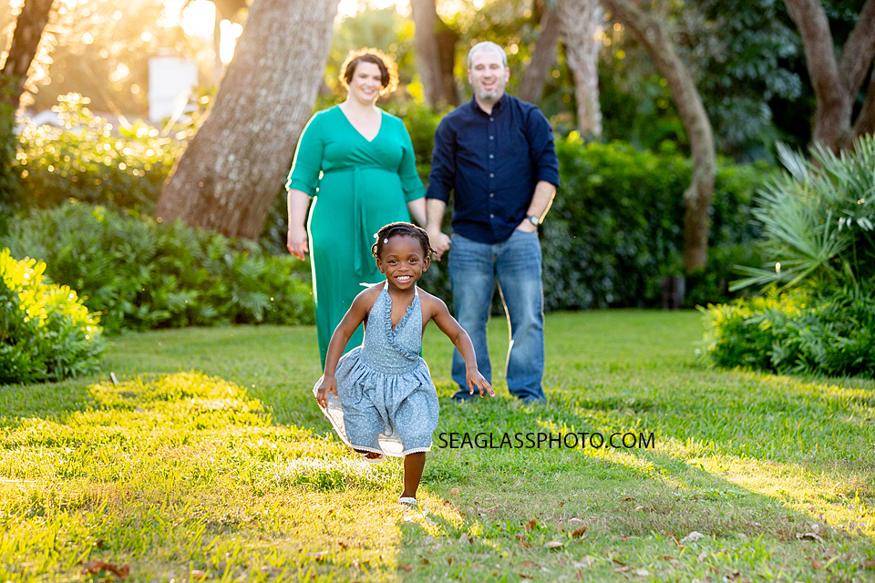 Little girl runs towards the camera while parents smile and watch during family photos in Vero Beach Florida