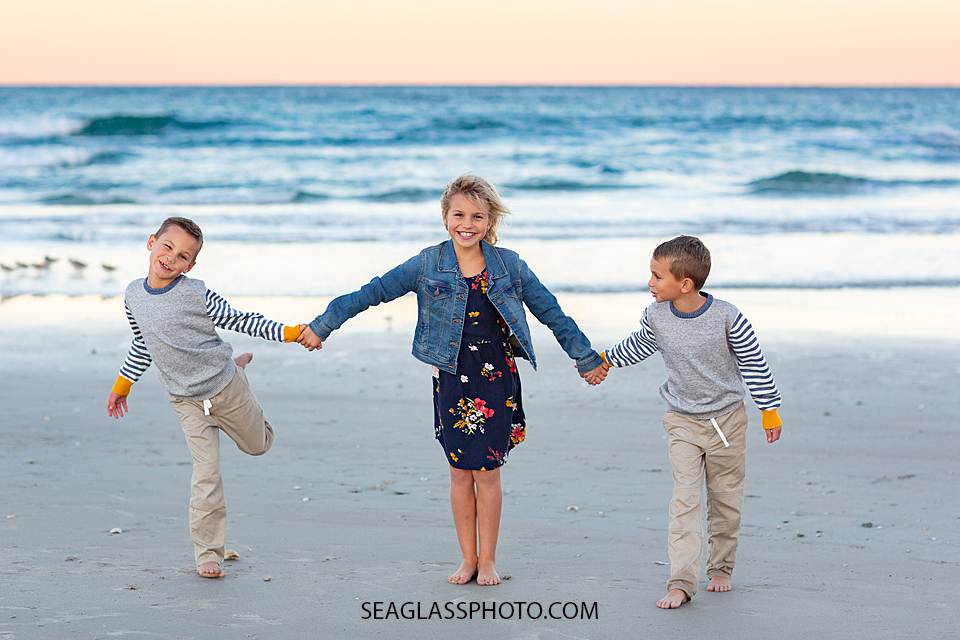 Three siblings walk away from the ocean smiling for the camera at the Fort Pierce Inlet during family photos