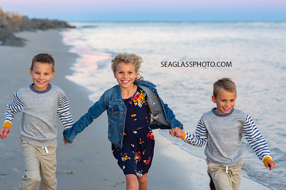 Three siblings holding hands walk on the beach at the Fort Pierce Inlet during family photos