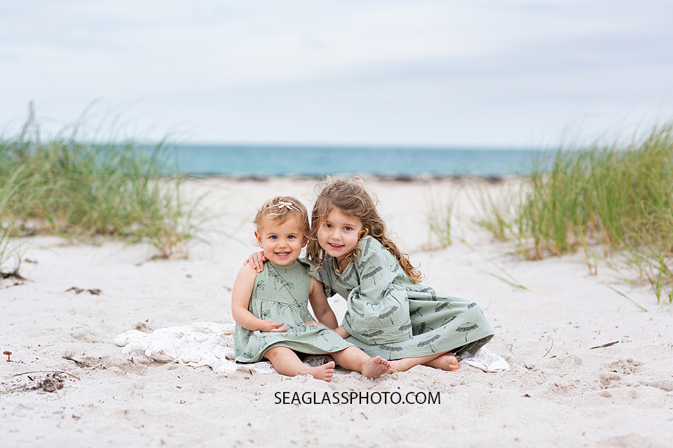Sisters sit on the beach during family photos in Vero Beach Florida