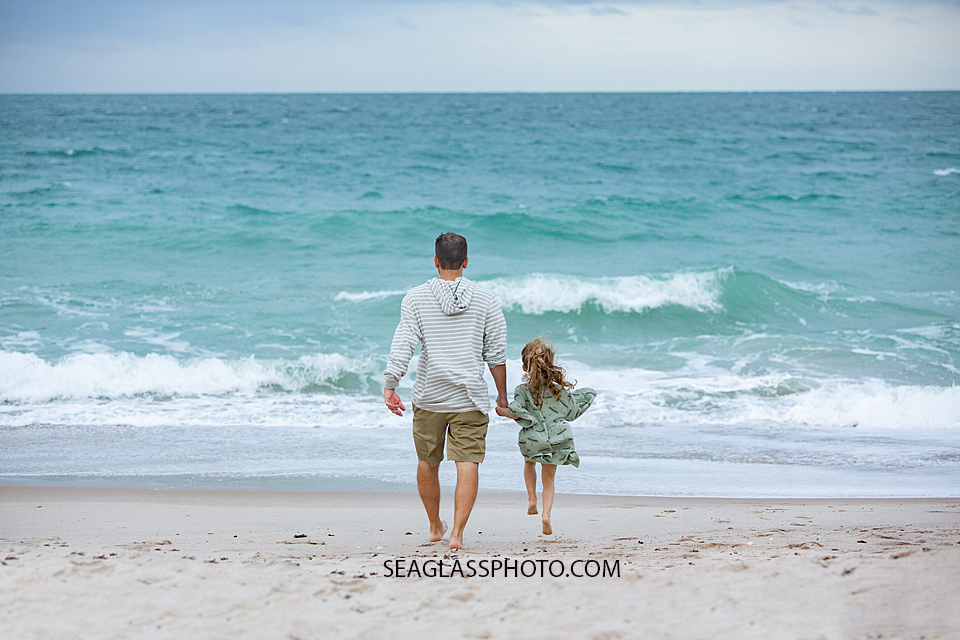 Father and daughter walk towards the ocean during family photos in Vero Beach Florida