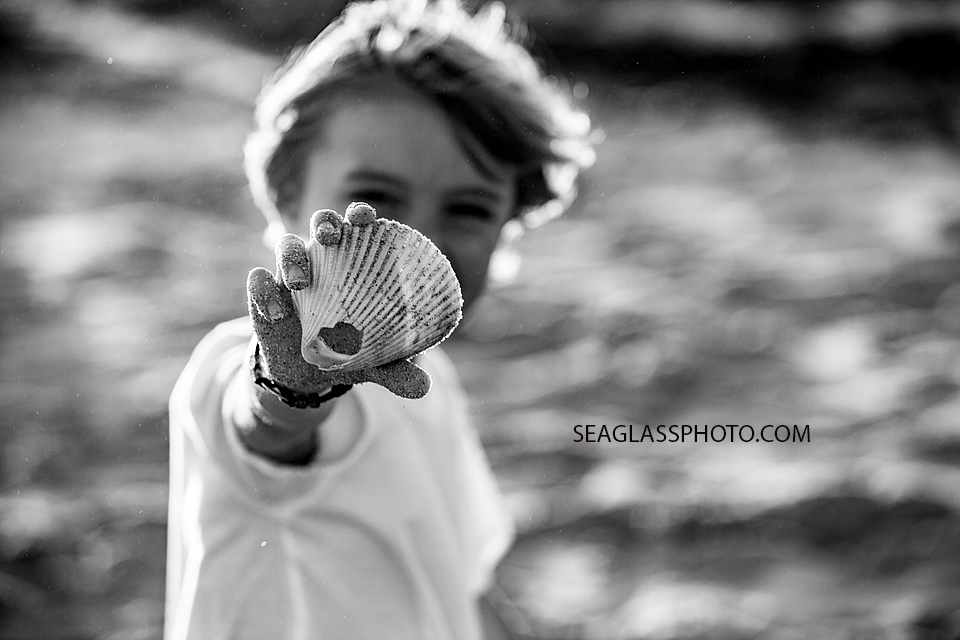 Black and white photo of young boy showing off a shell he found on the beach during family photoshoot in Vero Beach Florida