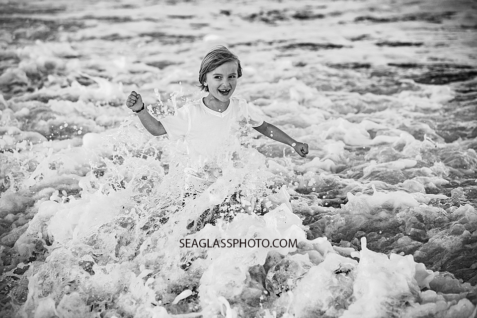 Black and white photo of young boy running in the water during family photoshoot in Vero Beach Florida