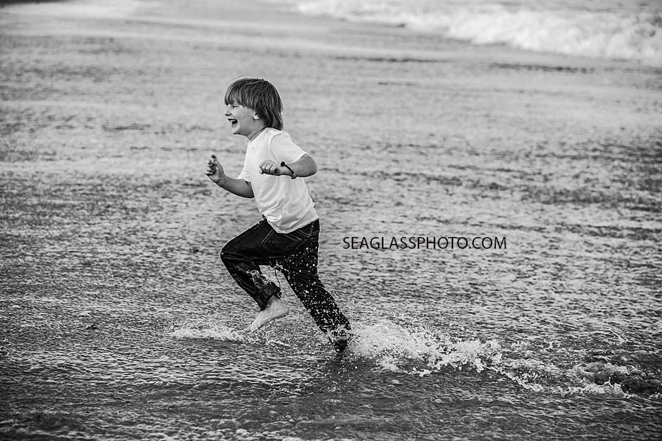 Black and white photo of young boy running away from the waves of the ocean during family photoshoot in Vero Beach Florida