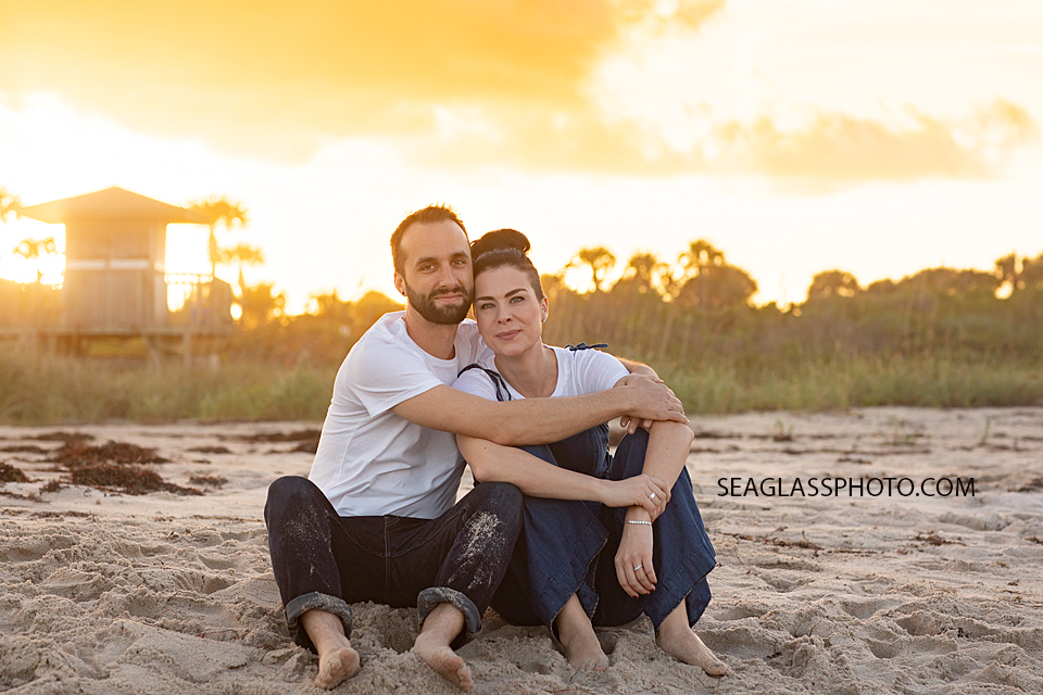Husband and wife sit in the sand admiring the ocean in front of them during family photoshoot in Vero Beach Florida