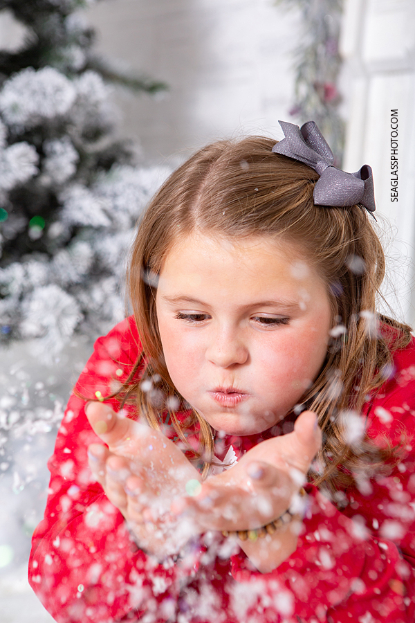 Young girl blowing snow into the camera during holiday family photos in Vero Beach Florida