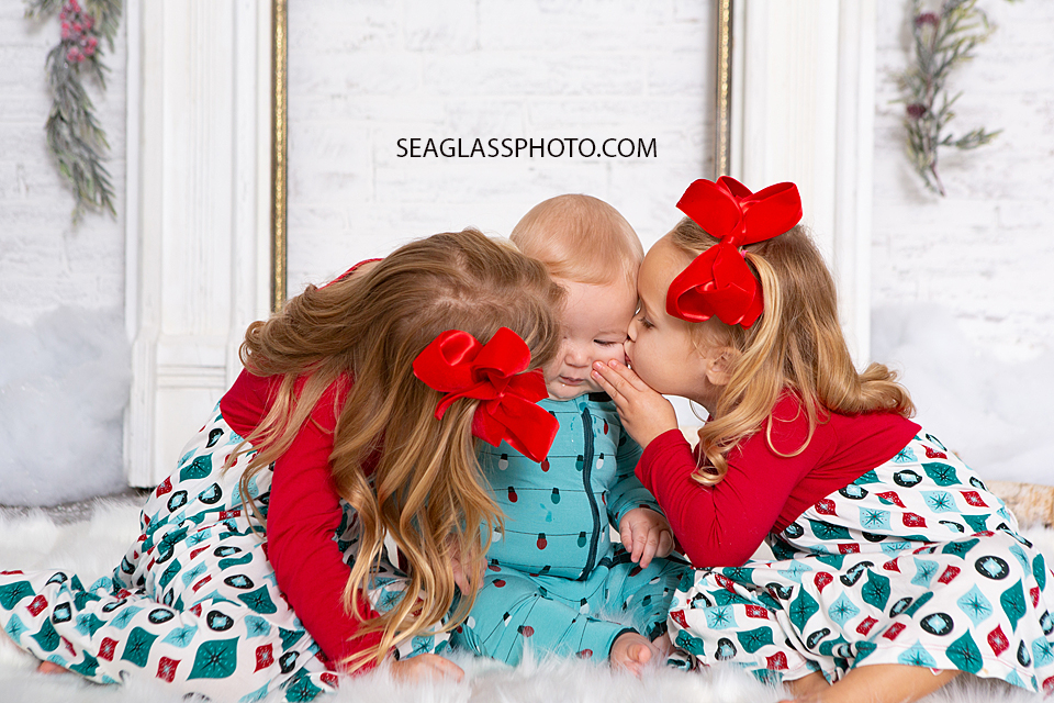 Close up of sisters kissing their little brother on his cheeks for Christmas photos in Vero Beach Florida