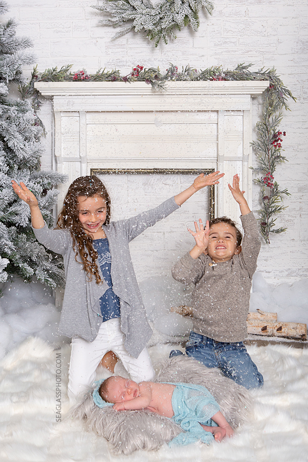 Siblings throw snow into the air while little baby brother sleeps during newborn photoshoot in Vero beach Florida