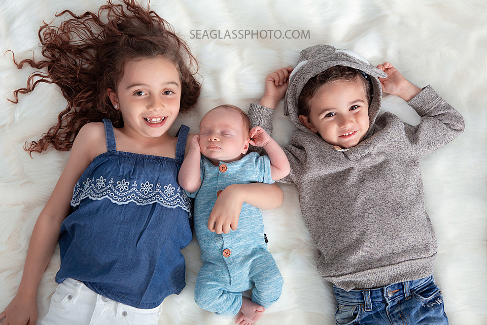 Three siblings lay down and smile during newborn photoshoot in Vero beach Florida