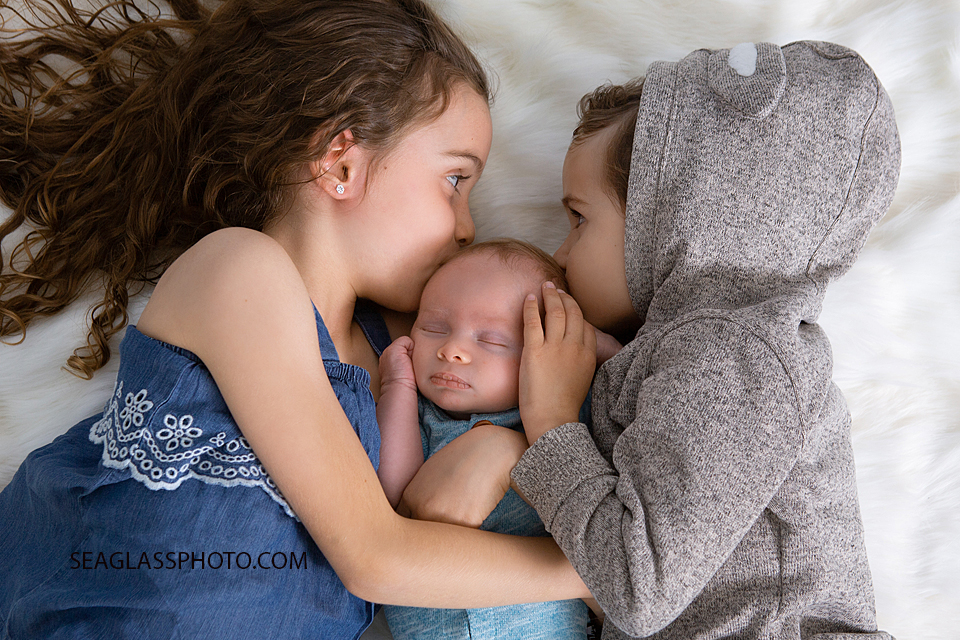 Big brother and sister give this new little guy kisses on the head during newborn photoshoot in Vero beach Florida