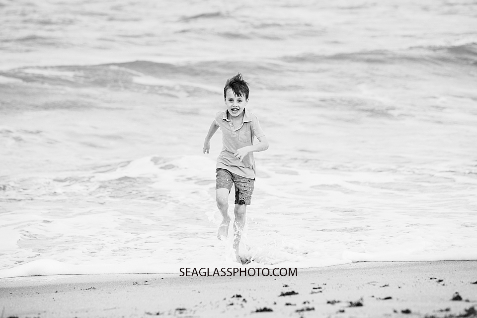 Black and white photo of a young boy running from the water on the beach during family photos in Vero Beach Florida