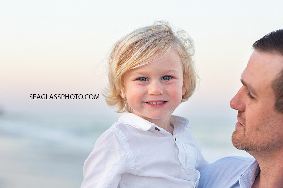 Close up of little boy smiling while dad holds him on the beach during their family photoshoot in Vero Beach Florida