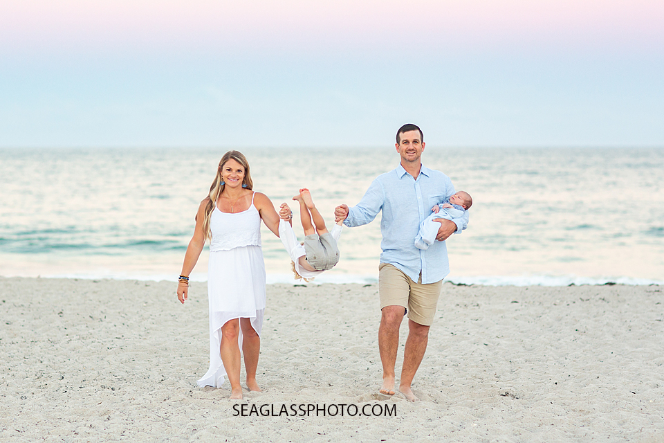 Parents walk as their son plays between them on the beach during their family photoshoot in Vero Beach Florida