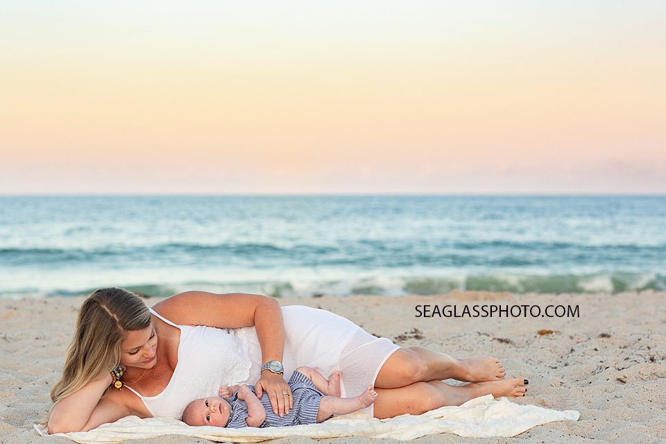 Mother lays by her two month old sons on a blanket on the beach during their family photoshoot in Vero Beach Florida