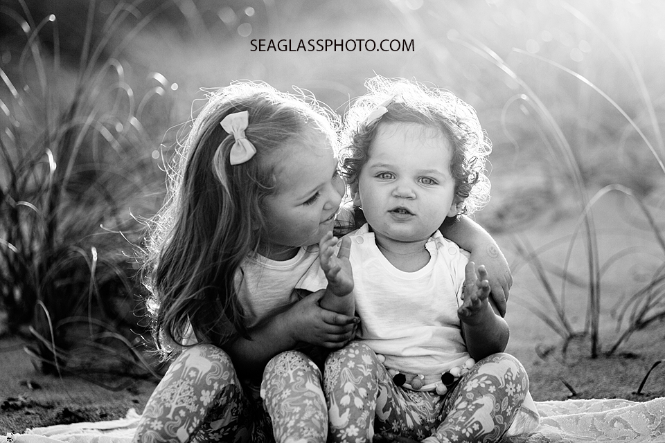 Black and white photo of a big sister hugging her little sis on the beach during their family photo shoot in Vero Beach Florida