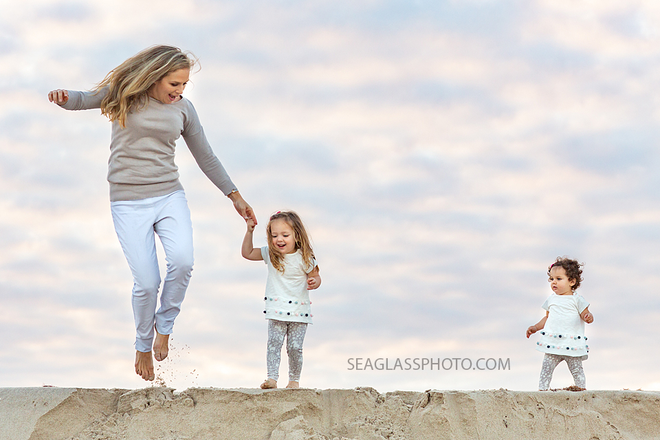 Mom jumps down a step on the beach with her daughters during their family photo shoot in Vero Beach Florida