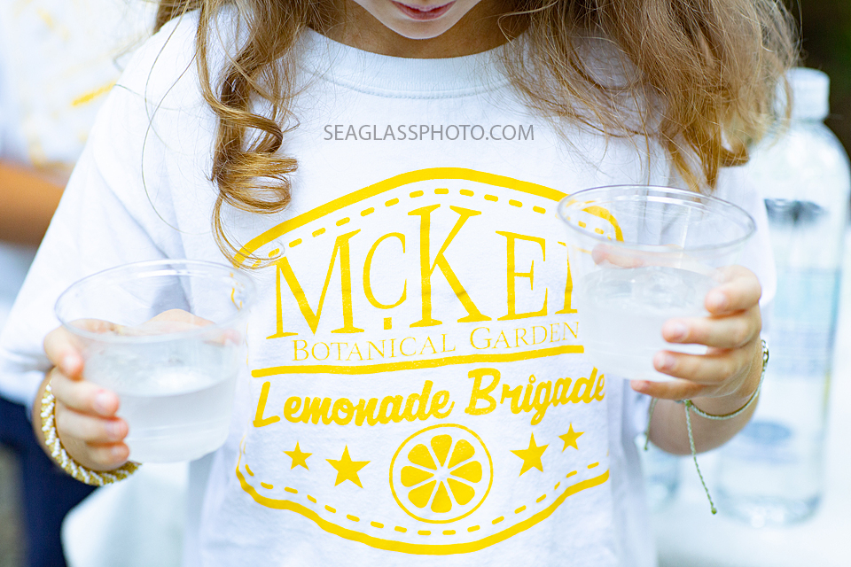 Close up of a young girl carrying waters and wearing the lemonade stand tee shirt at McKee Gardens dinner held to preview the new children center photographed by a Vero Beach Florida photographer