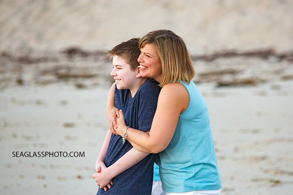 Mother hugs her oldest sun on the beach while watching the sunrise during a family photoshoot in Vero Beach Florida