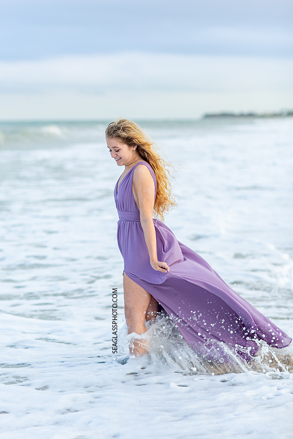 Senior walking the the water as it splashes during her senior photoshoot in Vero Beach Florida